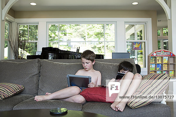Brothers using tablet computer while sitting on sofa at home