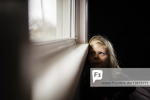 Nachdenkliches Mädchen  das zu Hause sitzend durchs Fenster schaut
