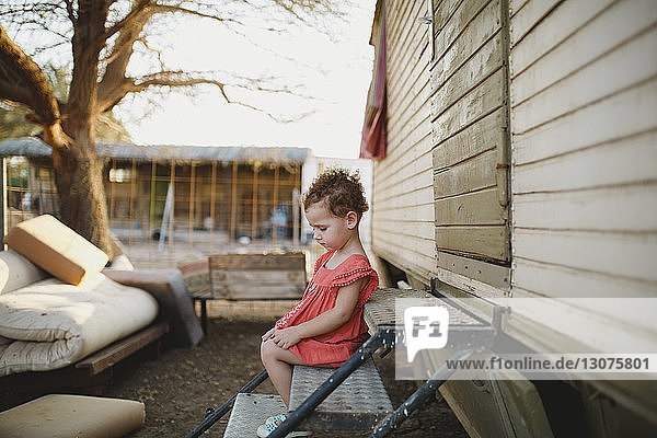 Side view of cute girl sitting on metallic steps at farm