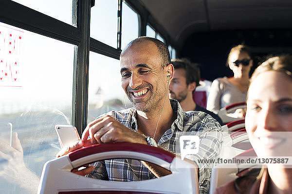 Glücklicher Mann benutzt Mobiltelefon während der Fahrt im Reisebus