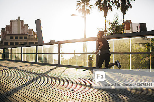 Rückansicht einer Frau  die bei Sonnenuntergang auf der Brücke joggt