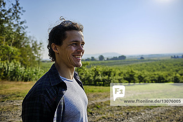 Lächelnder Landwirt schaut weg  während er im Obstgarten vor dem klaren Himmel steht