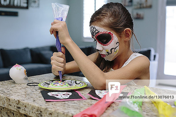 Girl with face paint decorating plate while sitting at table