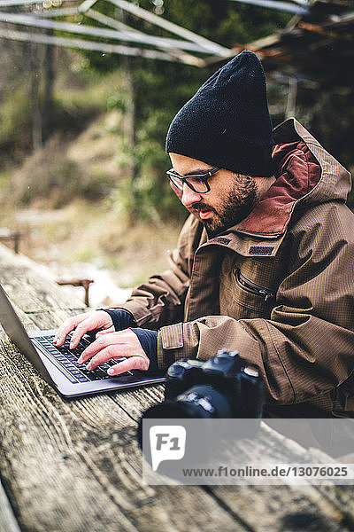 Male hiker using laptop computer by camera on table in forest