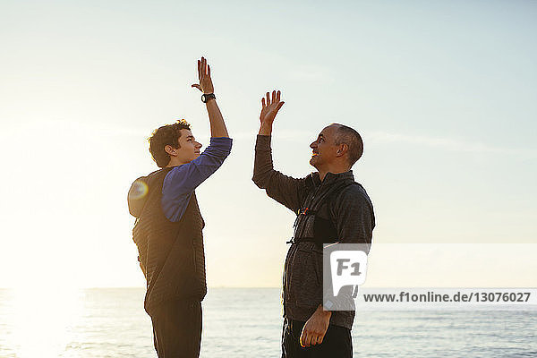 Happy father and son having high-five against sea and sky during sunset