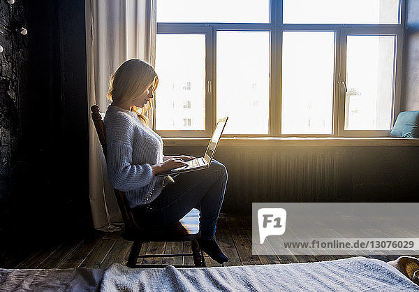 Seitenansicht einer Teenagerin  die einen Laptop benutzt  während sie zu Hause auf einem Stuhl sitzt