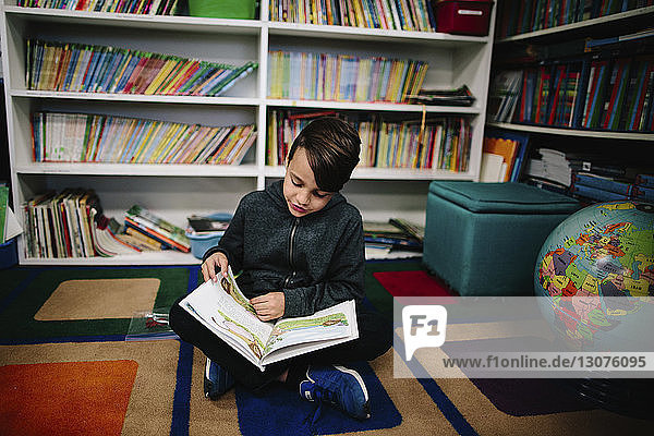 Junge lernt  während er gegen Bücherregale in der Bibliothek sitzt