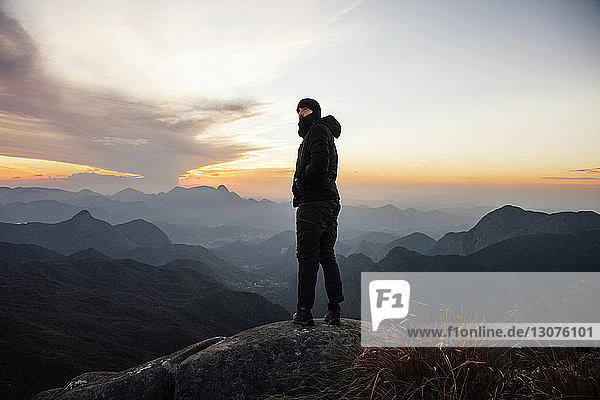 Man looking away while standing on mountain during sunset