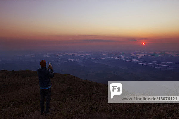 Man photographing scenic view of sunset while standing on mountain