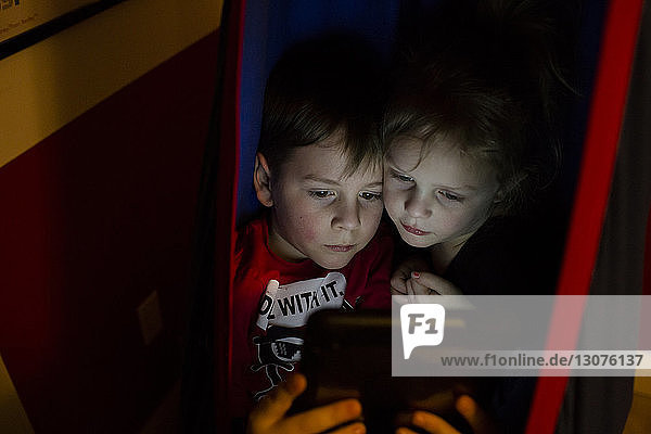 Siblings using tablet computer in tent at home