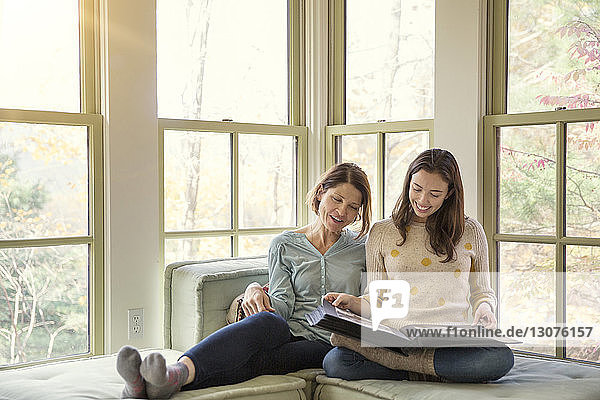 Smiling mother and daughter looking at photo album in living room