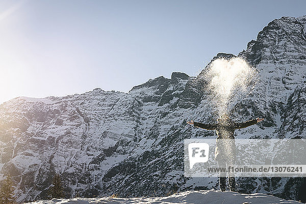 Frau wirft Schnee  während sie am sonnigen Tag auf Berg gegen klaren Himmel steht