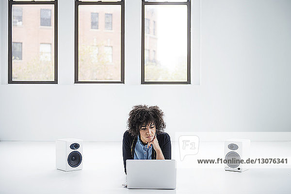 Geschäftsfrau benutzt Laptop  während sie inmitten von Lautsprechern auf dem Boden im Büro liegt
