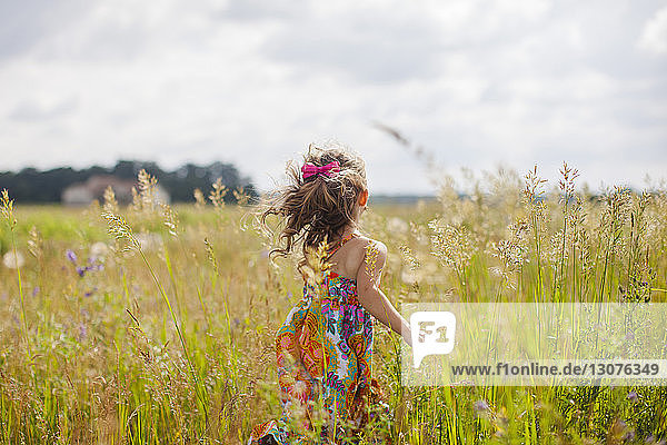 Rückansicht eines Mädchens mit Laufen auf Grasfeld gegen den Himmel