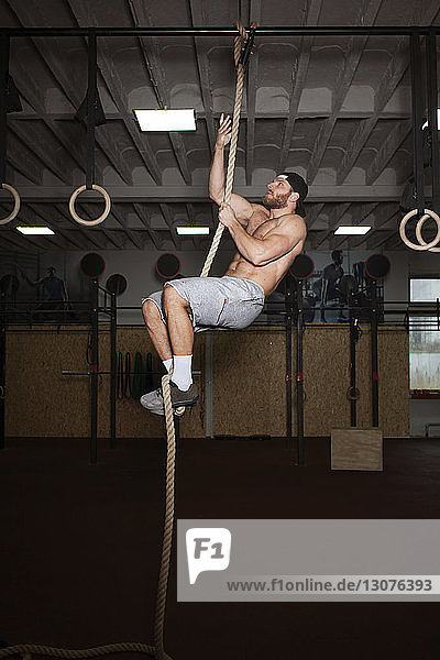 Man climbing on rope while exercising in gym