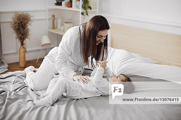 Happy mid adult woman looking at baby boy lying in bed at home