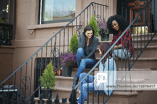 Freunde unterhalten sich  während sie auf Stufen vor dem Haus sitzen