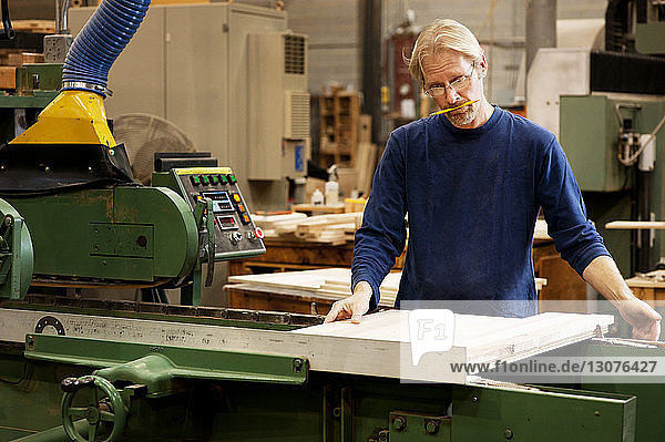 Seriöser Schreiner mit Maschinen auf Holzbrettern in der Werkstatt