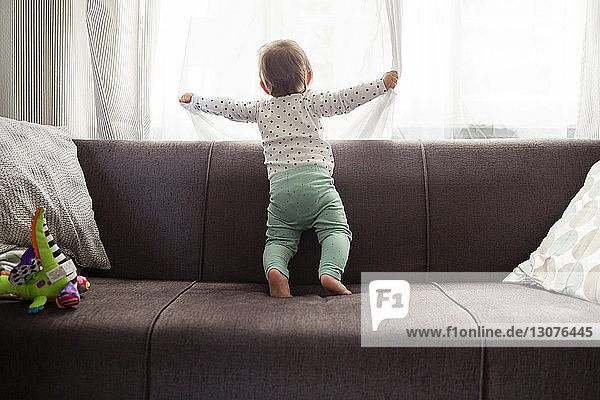 Kleines Mädchen schaut durchs Fenster  während es zu Hause auf dem Sofa steht
