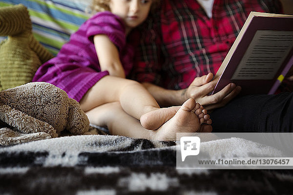 Ausgeschnittenes Bild eines Mädchens  das beim Vater sitzt und zu Hause ein Buch hält