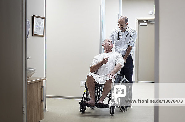 Arzt trägt Patient im Rollstuhl auf dem Korridor