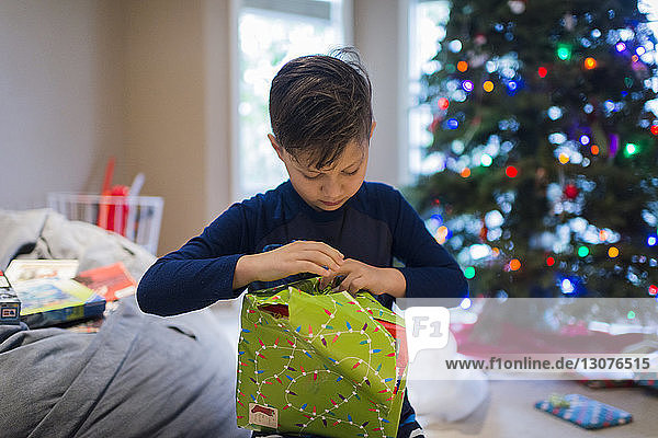 Junge packt Weihnachtsgeschenk ein  während er zu Hause sitzt