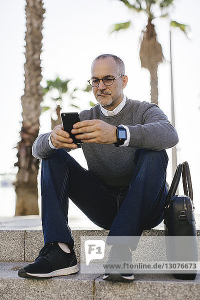Seriöser Geschäftsmann benutzt Smartphone  während er auf Treppen in der Stadt sitzt