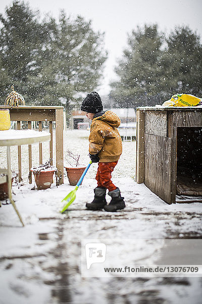 Seitenansicht eines Jungen  der im Hof Schnee mit einer Schaufel räumt