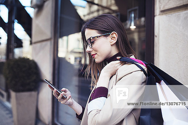 Frau mit Einkaufstaschen  die ein Mobiltelefon benutzt  während sie am Gebäude steht
