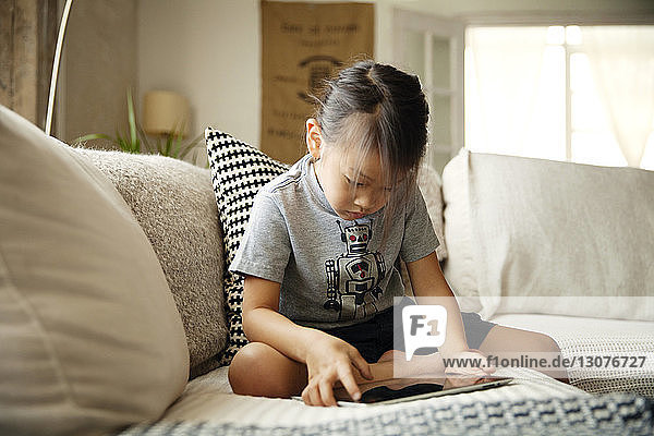 Neugieriges Mädchen benutzt Tablet-Computer  während sie zu Hause auf dem Sofa sitzt