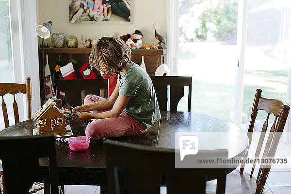 Girl making gingerbread house on table at home
