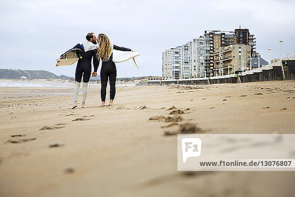 Paar küsst sich beim Halten von Surfbrettern am Strand
