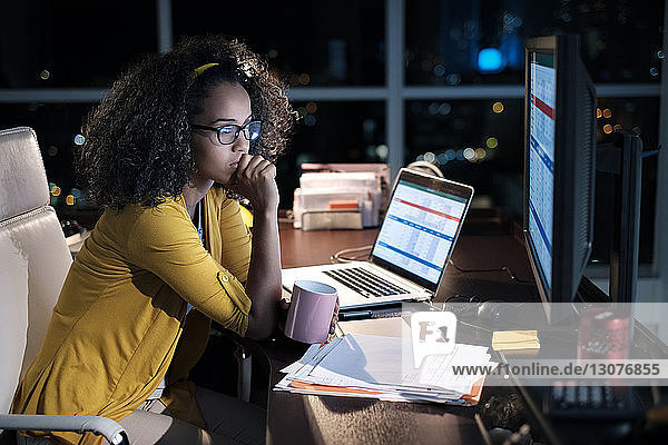 Nachdenkliche Geschäftsfrau hält Kaffeetasse  während sie nachts im Büro auf einem Stuhl sitzt