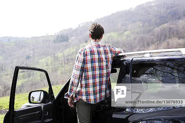Rückansicht eines Mannes  der vor einem Auto auf einem Berg steht