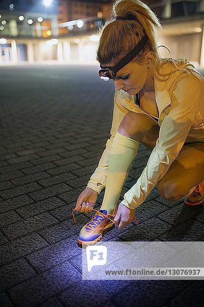 Weibliche Sportlerin bindet nachts auf dem Gehweg die Schnürsenkel