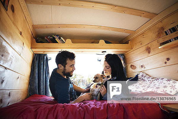 Couple looking at dog while relaxing on bed in camper van