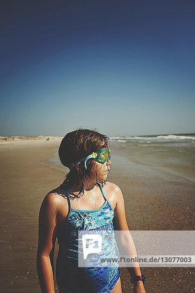 Girl wearing swimming goggles while looking away at St. Augustine Beach against clear sky during sunny day