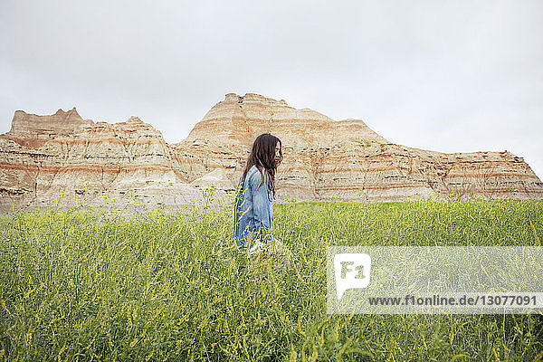Side view of woman walking on grassy field against mountains