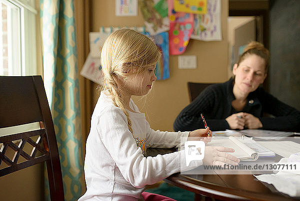 Mother assisting girl writing homework at table
