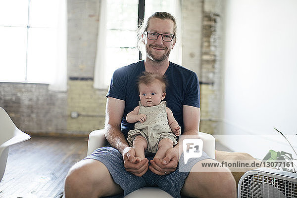 Porträt eines glücklichen Vaters  der mit seiner Tochter zu Hause auf einem Stuhl sitzt