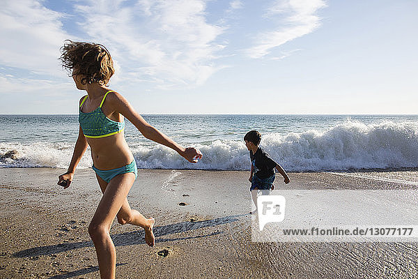 Girl and boy running from rushing waves at beach