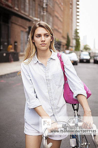 Nachdenkliche Frau mit Fahrrad auf der Straße in der Stadt
