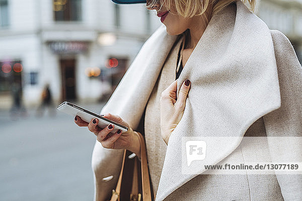Ein Teil der Frau benutzt ein Smartphone  während sie auf der Straße in der Stadt steht