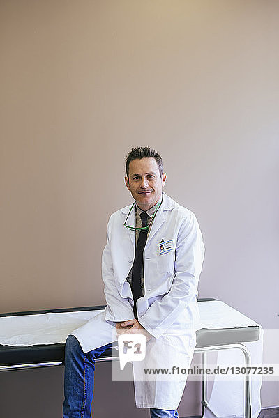 Portrait of smiling doctor sitting on bed against wall