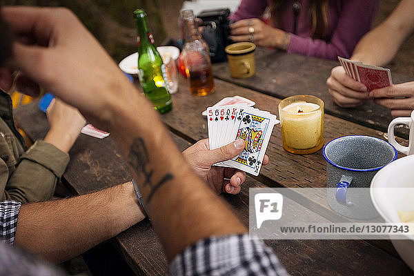 Ausgeschnittenes Bild von Freunden beim Kartenspielen am Picknicktisch im Wald