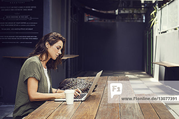 Seitenansicht einer Frau mit Laptop im Straßencafé