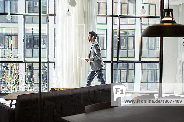 Side view of businessman with documents walking by window in office
