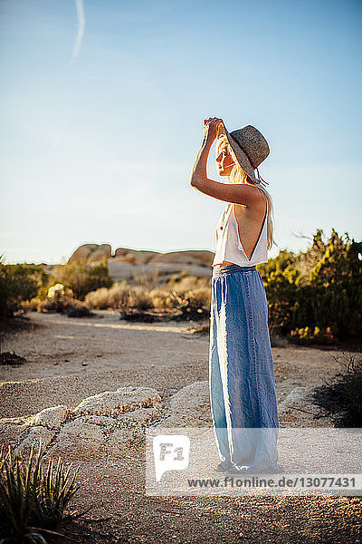 Frau schaut weg  während sie auf dem Feld im Joshua-Tree-Nationalpark vor blauem Himmel steht