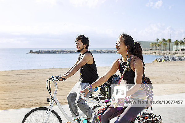 Sporty couple riding bicycles on road by beach