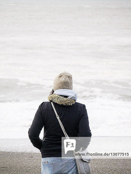 Rückansicht eines am Strand stehenden Teenagers in warmer Kleidung